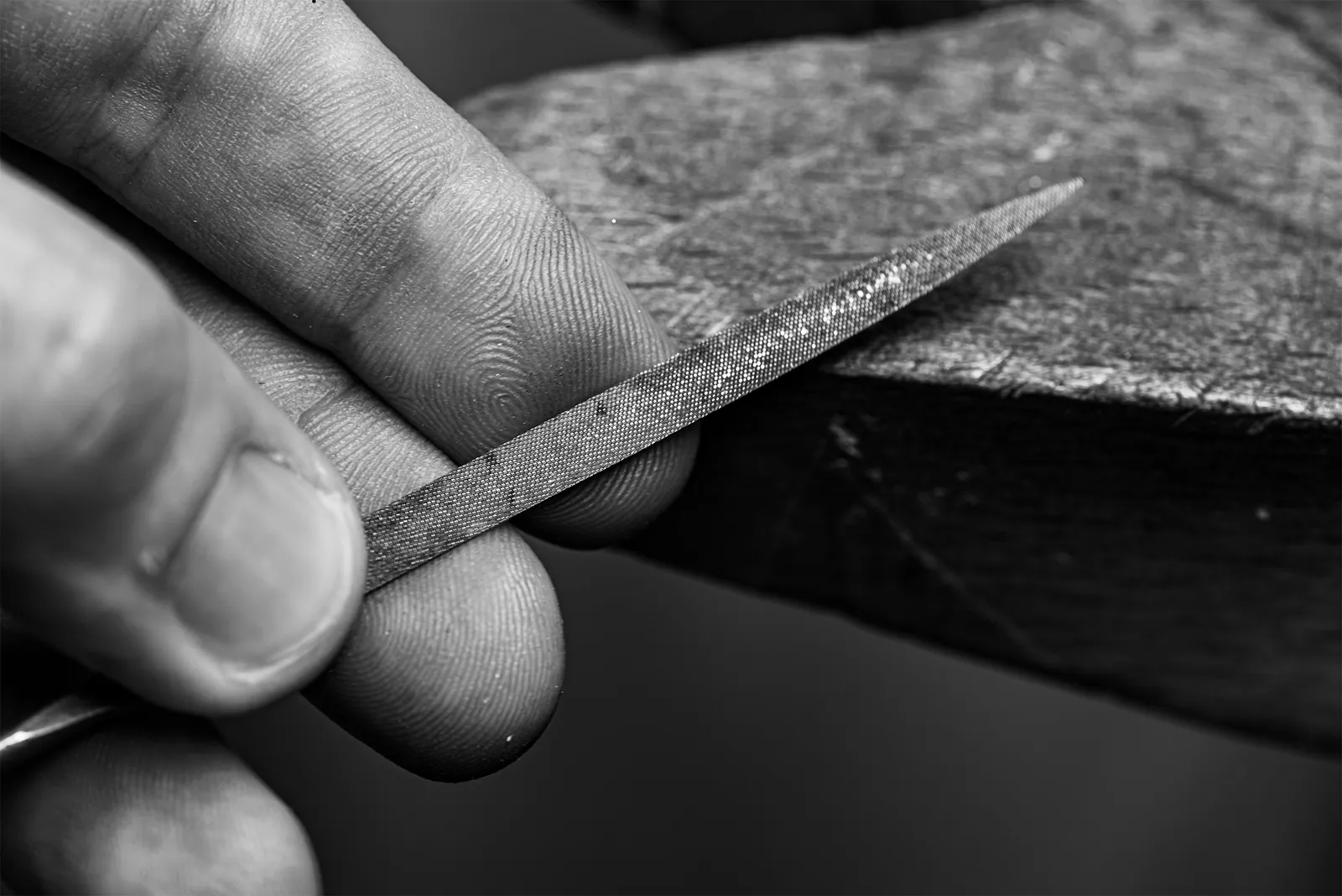 Hand eines Goldschmieds mit einer Feile an der Werkbank